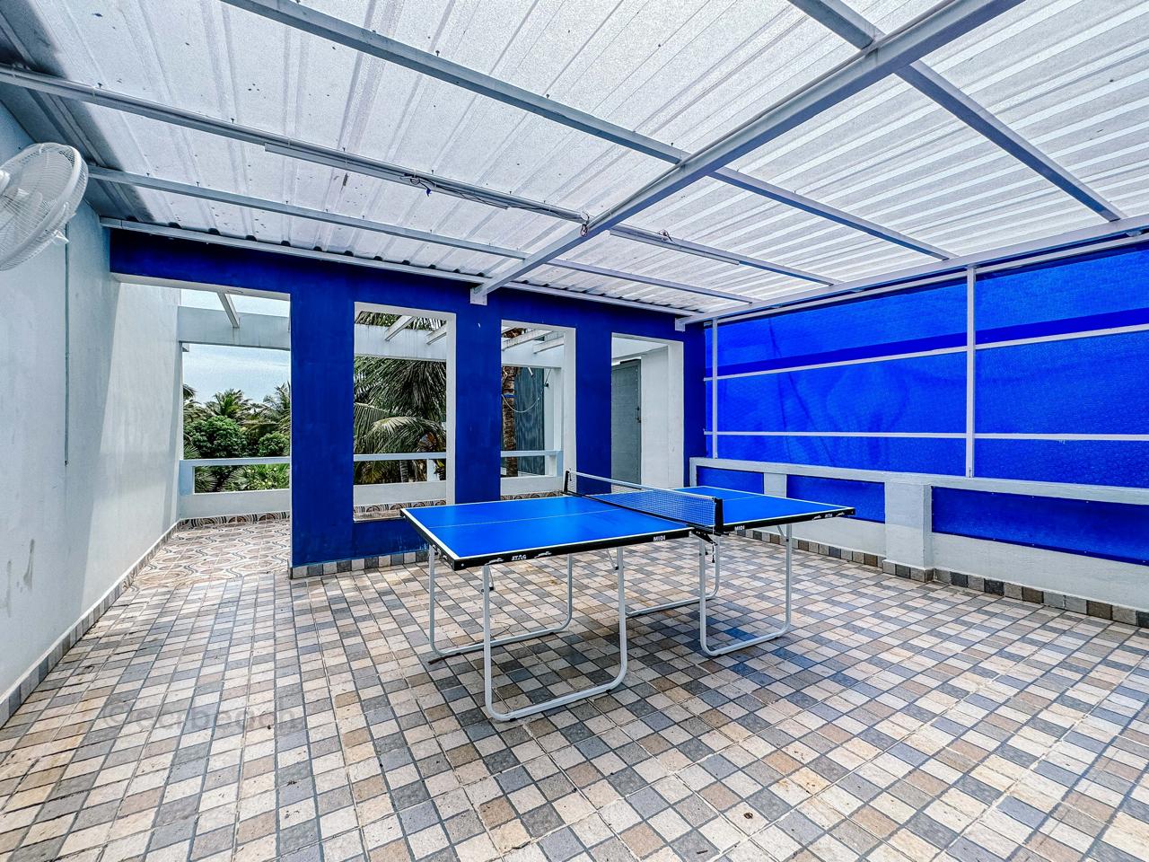 A blue table tennis table set up in a covered outdoor patio area with tiled flooring.