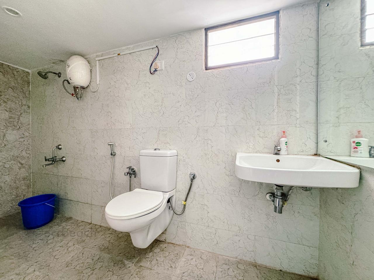 A tiled bathroom featuring a toilet, wall-mounted sink, shower fixture, and water heater.