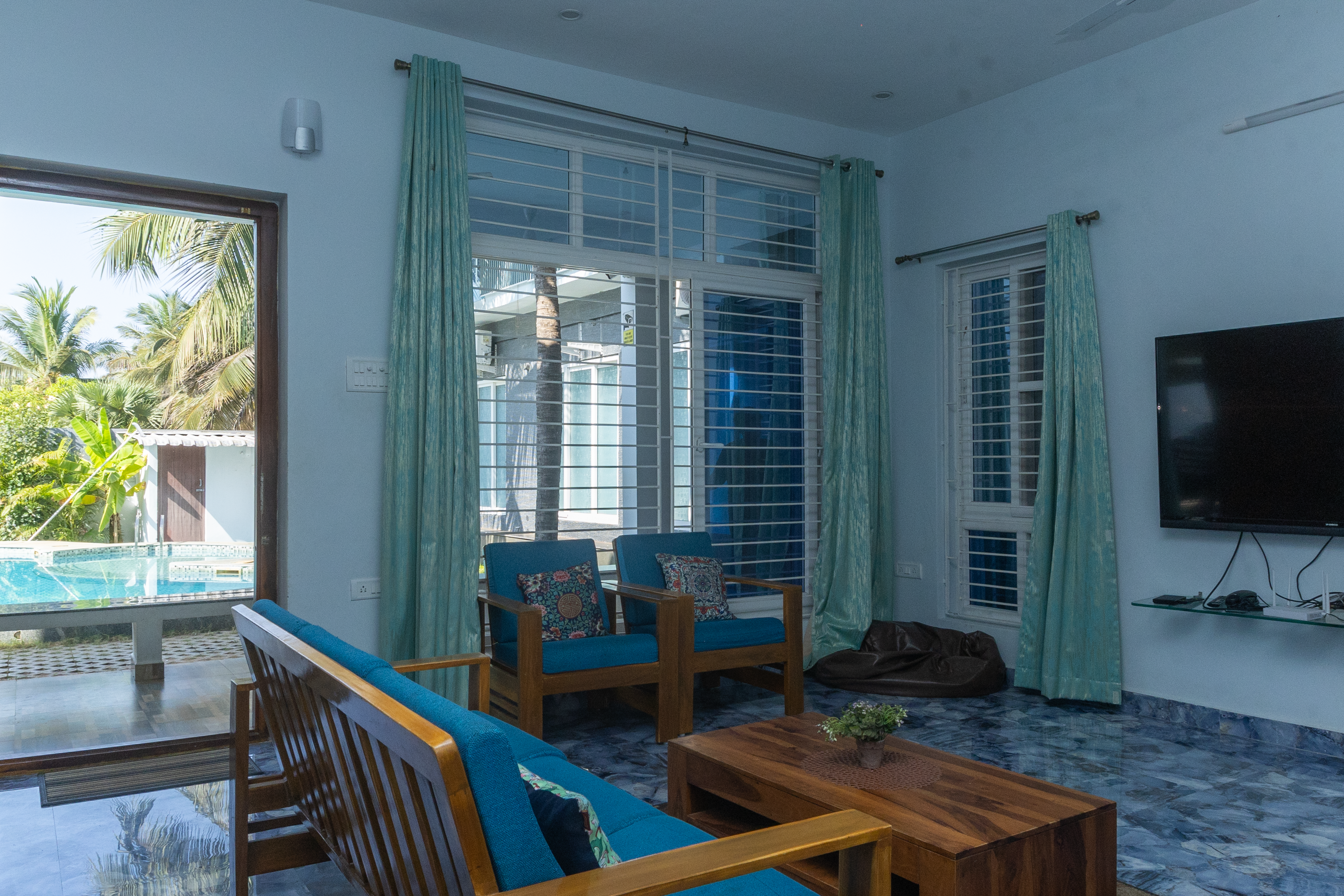 A modern living area with blue wooden armchairs, a sofa, coffee table, and pool view.