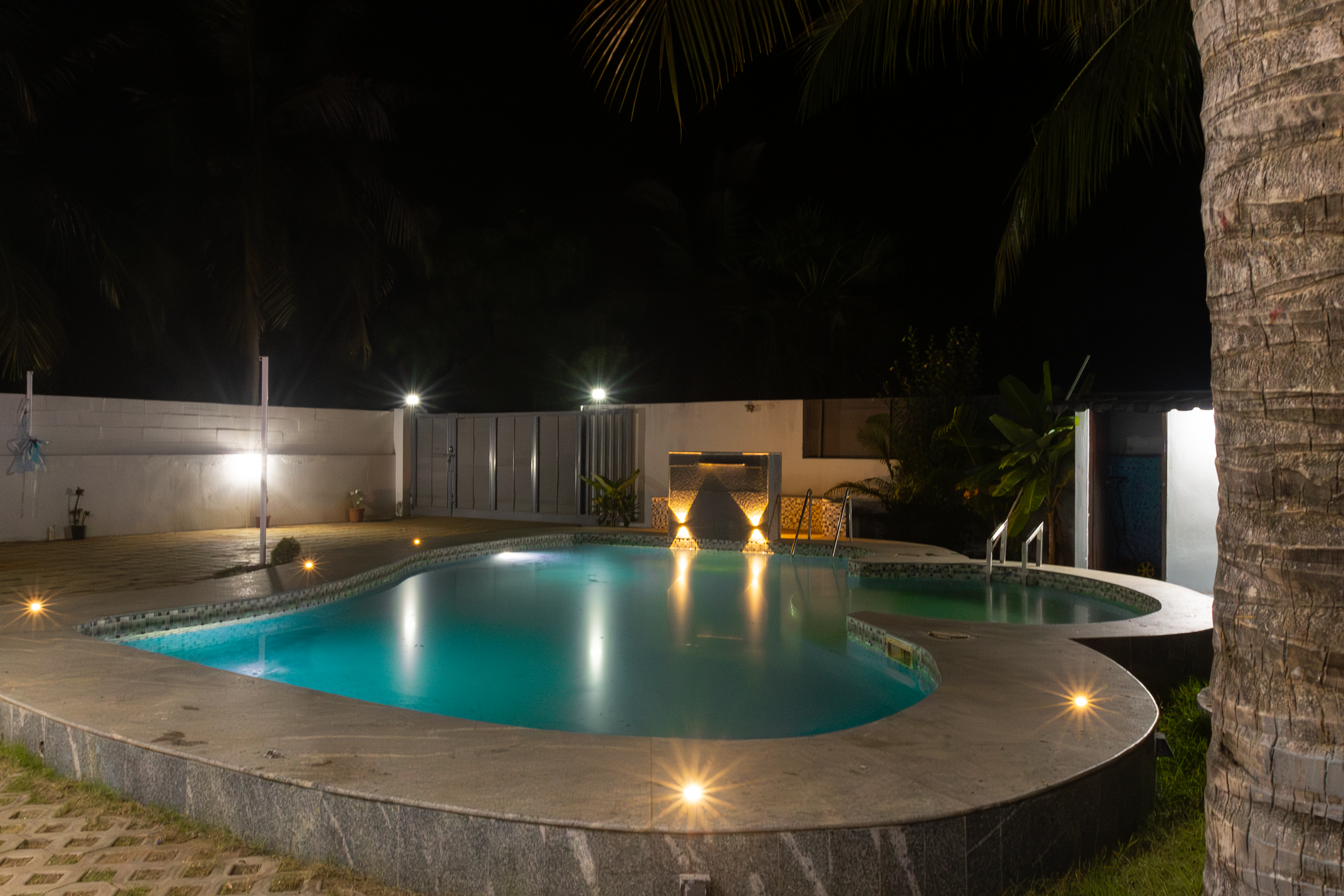 An outdoor swimming pool illuminated at night with deck lights and underwater lighting.