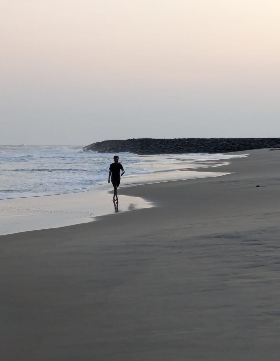 A person walking along a sandy beach near gentle ocean waves at twilight.