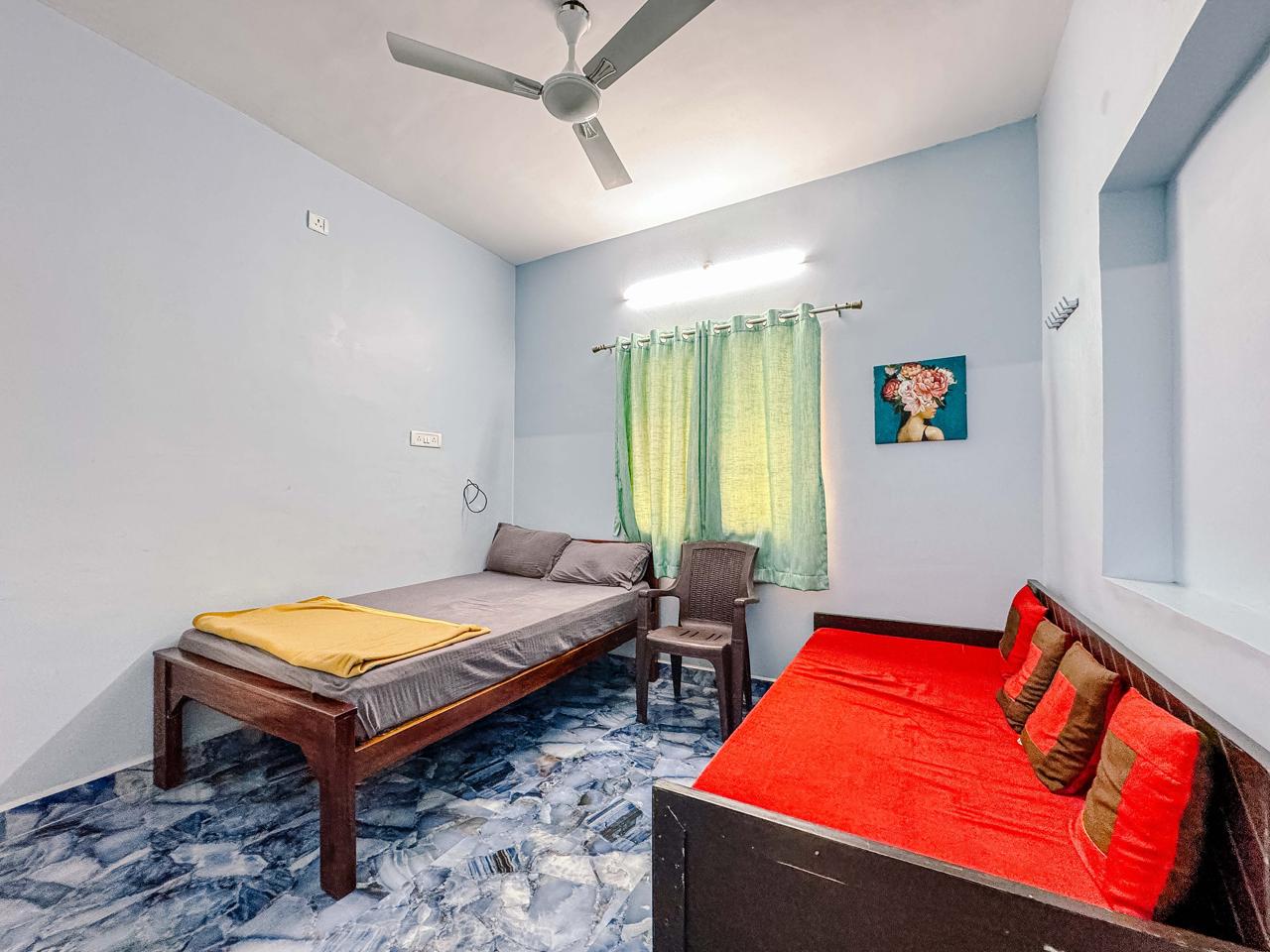 A simple bedroom with a single bed, red daybed, green curtains, and blue tiled floor.