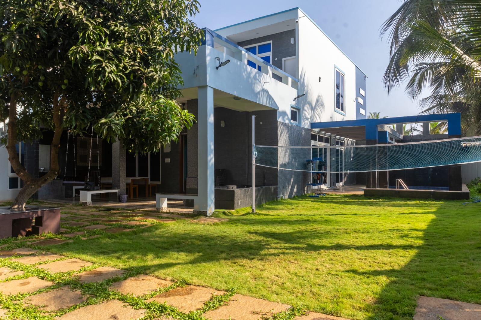Exterior view of a modern two-story light blue villa with a spacious green lawn.