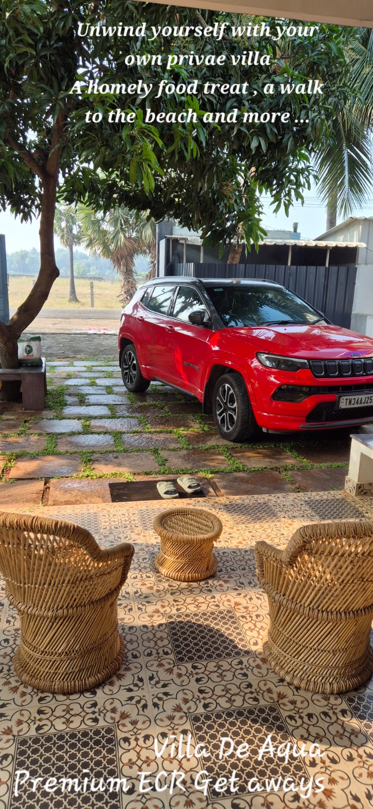 A red SUV parked in the driveway of a villa near wicker patio chairs.