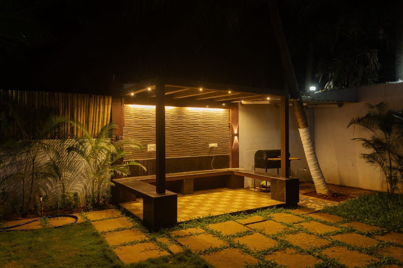 A cozy illuminated outdoor gazebo with seating area and garden at night.