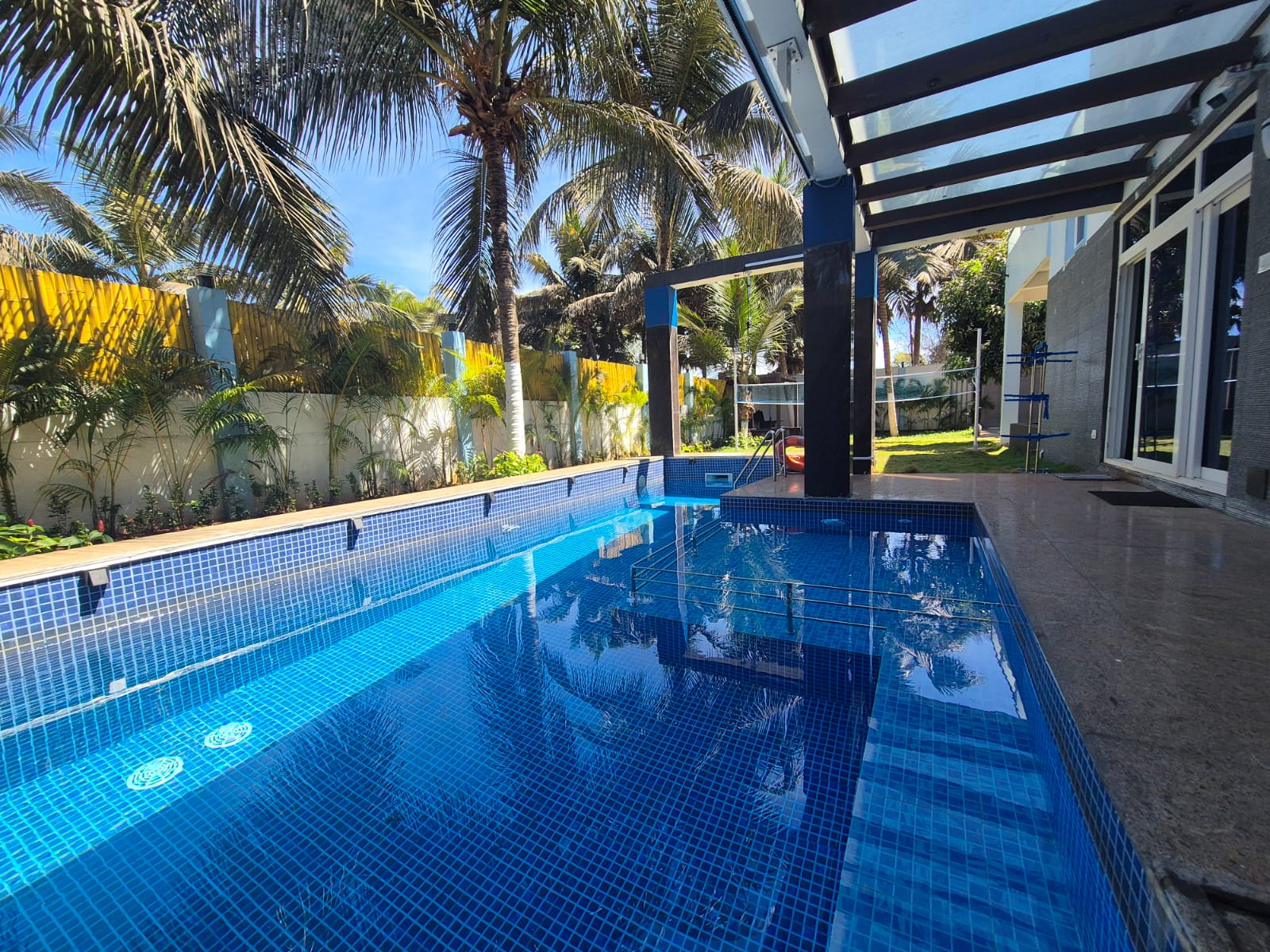 An outdoor blue tiled swimming pool with palm trees in the background next to a villa.