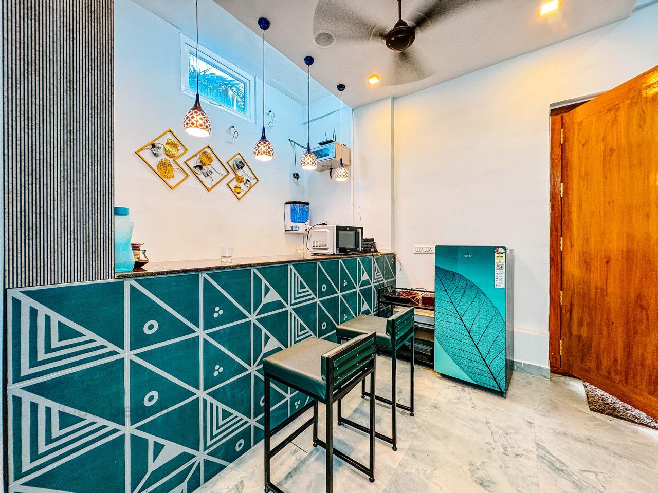A modern kitchen counter featuring geometric teal patterns, bar stools, pendant lights, and appliances.