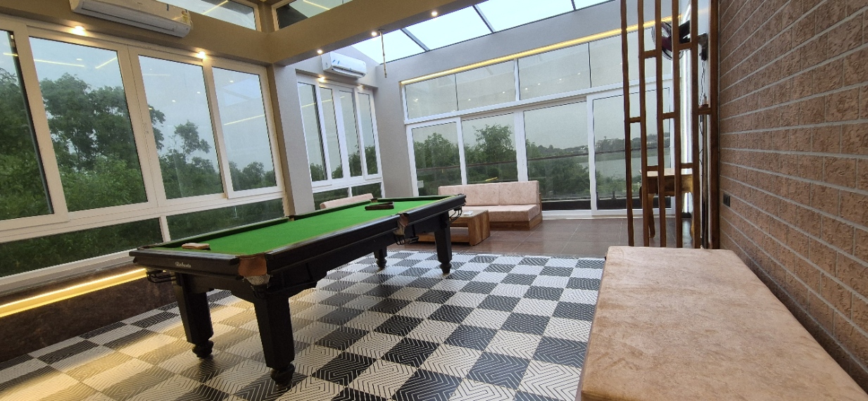 A sunroom featuring a billiards table on a checkered floor with large glass windows.
