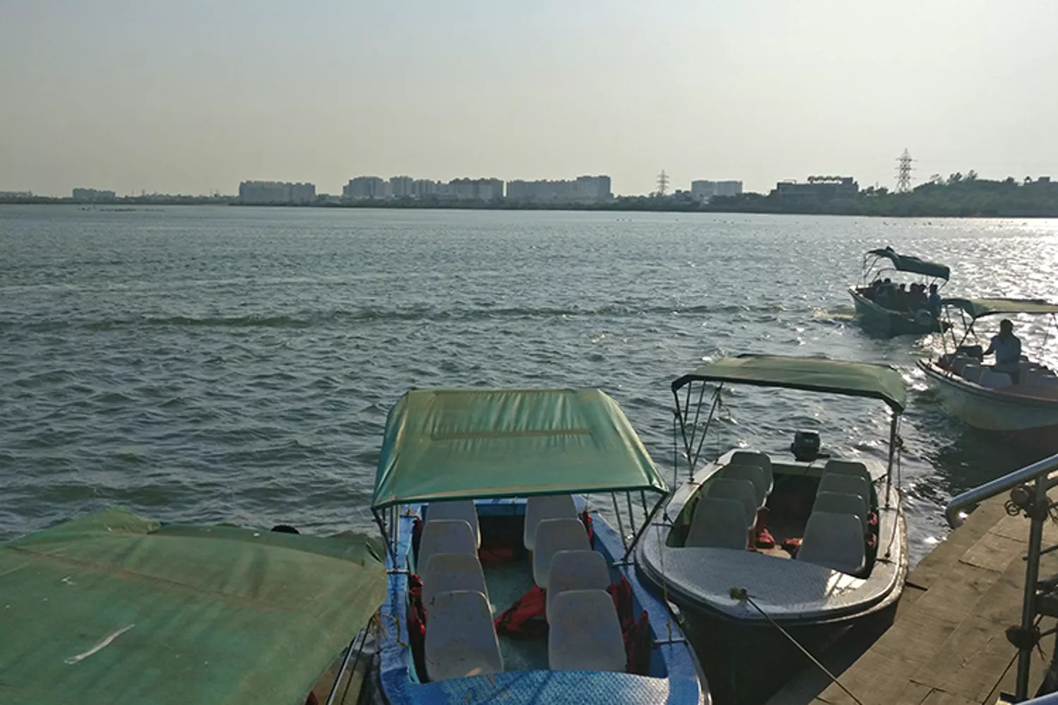 Small covered motorboats docked along a lake with a distant city skyline in the background.