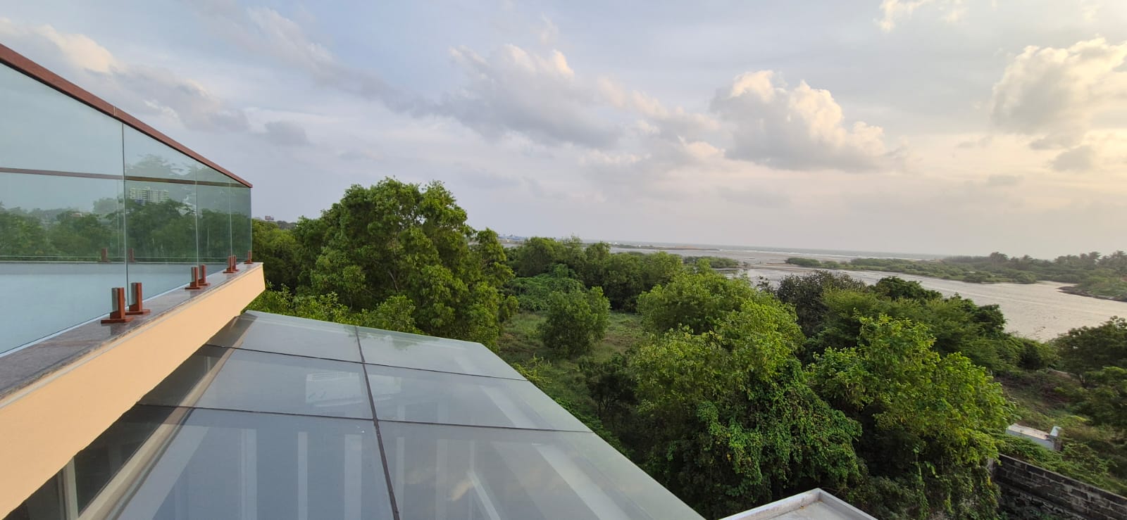 Panoramic view of lush green foliage and a body of water from a modern glass balcony.