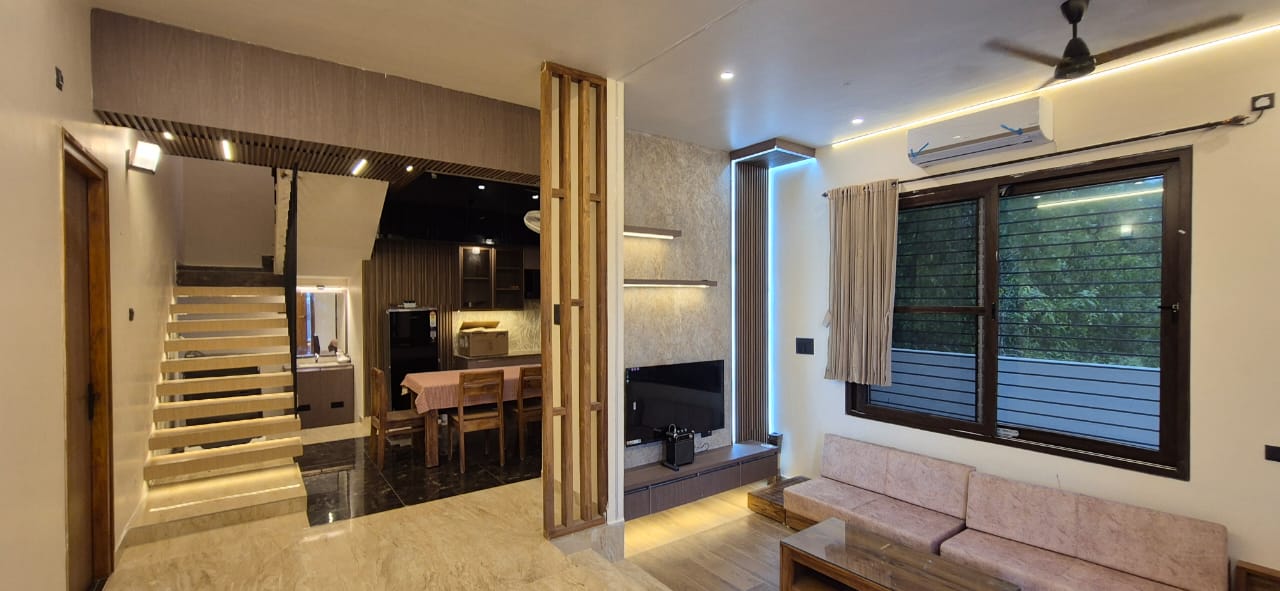 Modern interior living area with sofa, TV unit, wooden divider, and illuminated staircase.