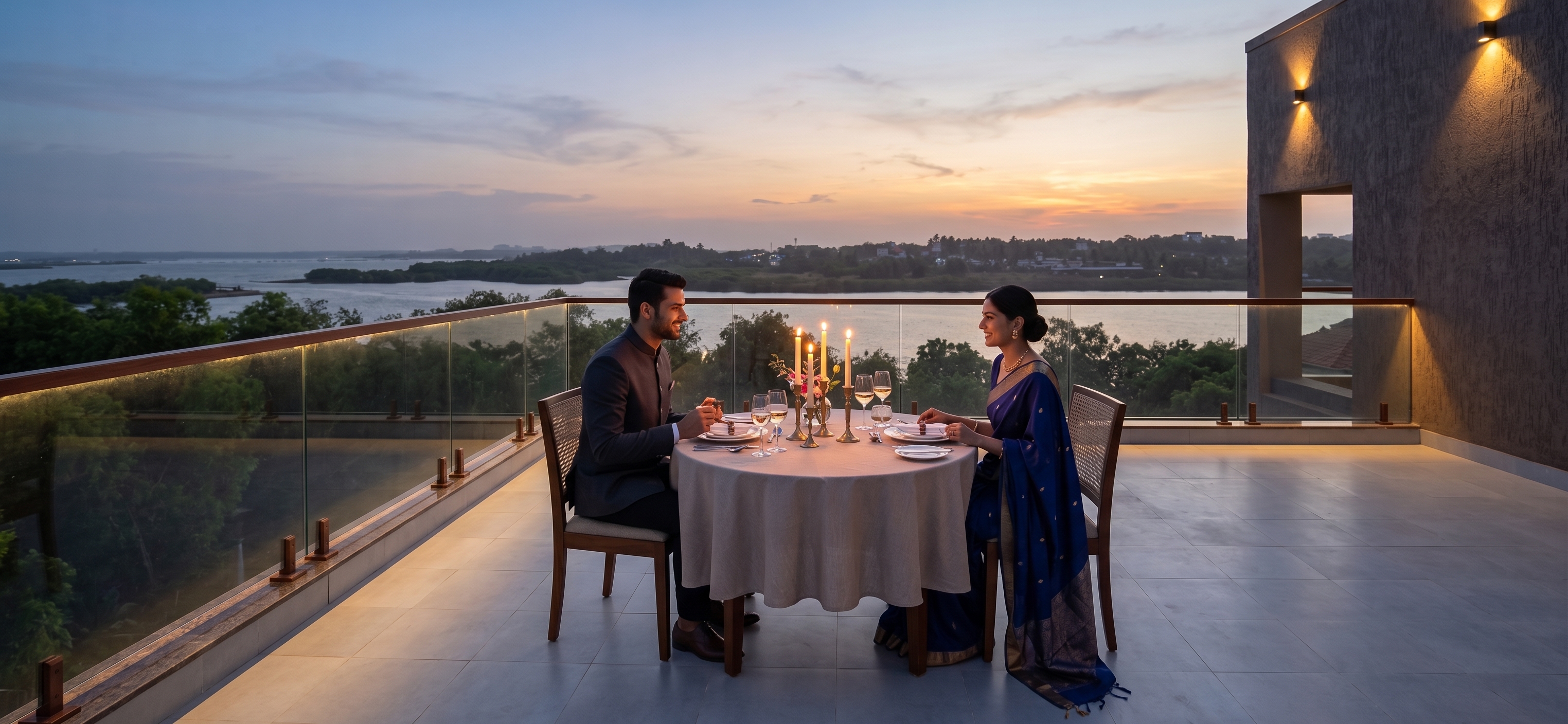A couple enjoying a romantic candlelit dinner on a rooftop balcony overlooking scenic waters at dusk.